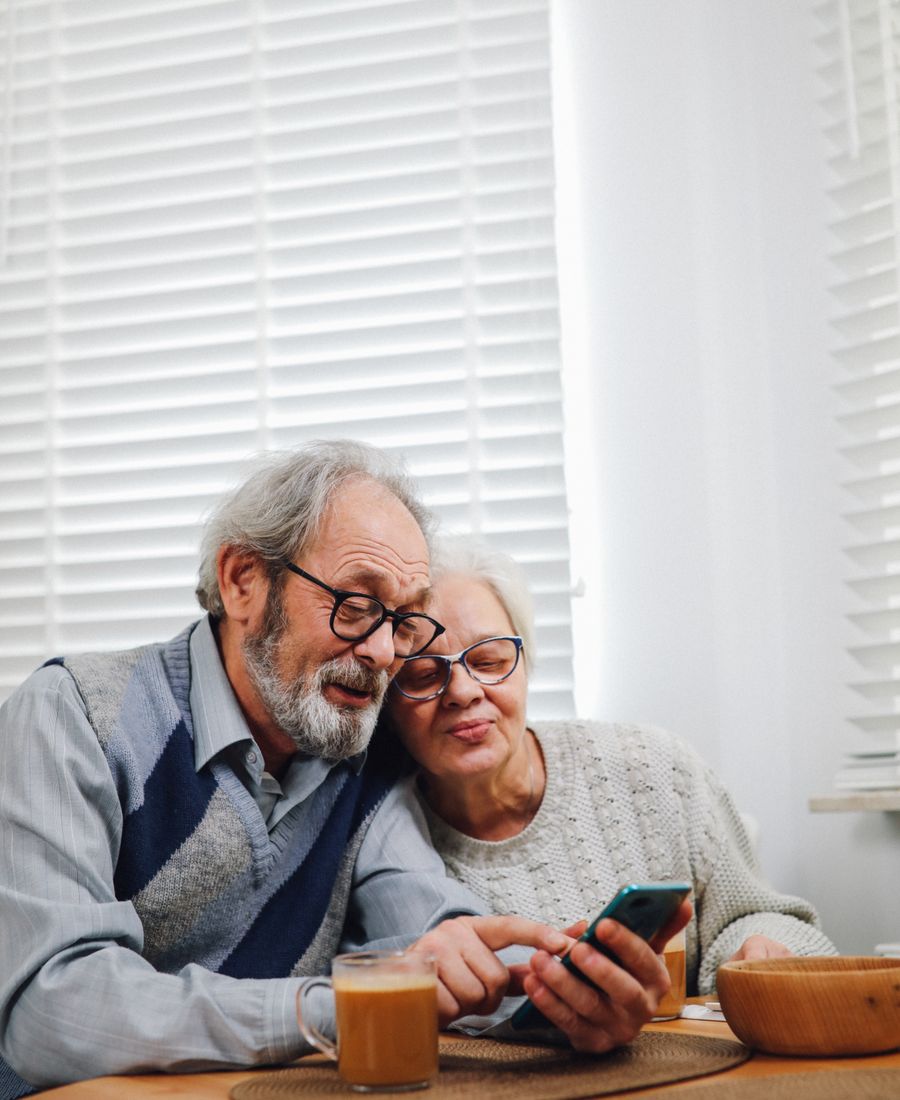 Casal de idosos sorrindo enquanto olha juntos a tela de um celular.