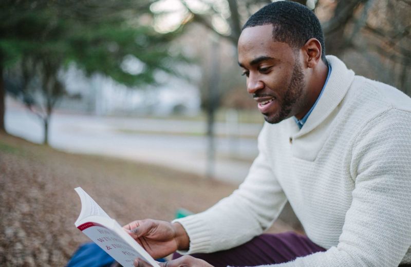 Homem sorrindo enquanto lê a Bíblia ao ar livre, pela manhã.