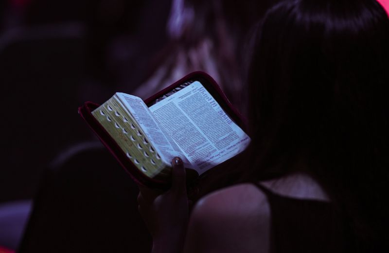 Pessoa lendo a Bíblia à noite, em um ambiente com pouca luz.